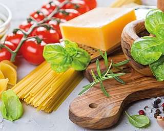 Frische Kräuter, Pasta, Tomaten und Käse auf einem Tisch.