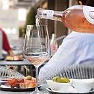 Eine Flasche Roséwein wird in ein Glas gegossen, mit Snacks im Hintergrund.