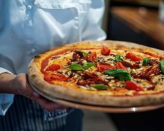 Eine Person hält eine frisch gebackene Pizza mit Tomaten und Basilikum.