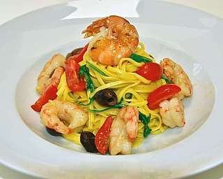 Piatto di pasta con gamberi, pomodorini e olive nere.